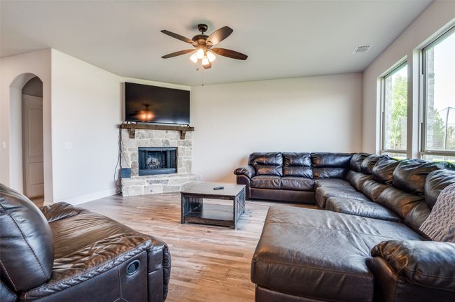 Living room with light wood-style floors, a ceiling fan, and a stone fireplace | Image 5