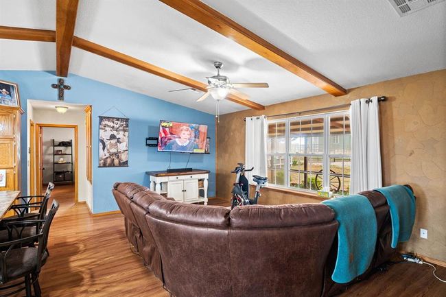 Living room with visible vents, baseboards, ceiling fan, wood finished floors, and vaulted ceiling with beams | Image 24