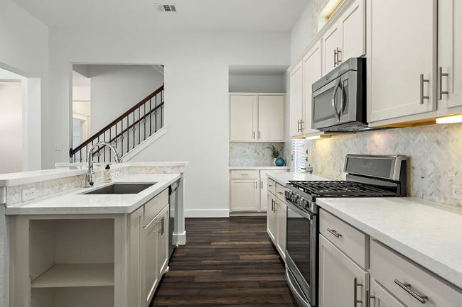 Kitchen with dark wood finished floors, tasteful backsplash, appliances with stainless steel finishes, a sink, and white cabinetry | Image 11