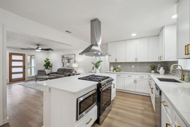 Kitchen with island range hood, appliances with stainless steel finishes, a sink, decorative backsplash, and light wood-style flooring | Image 13