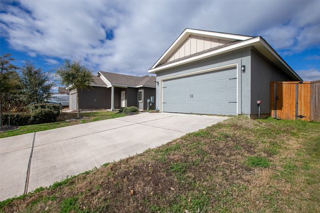 Ranch-style house featuring stucco siding, a gate, board and batten siding, concrete driveway, and a garage | Image 5