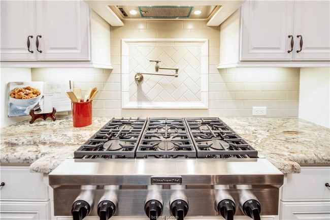 Kitchen with wall chimney exhaust hood, backsplash, light stone countertops, and white cabinetry | Image 12