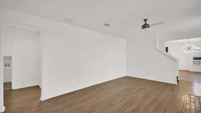 Unfurnished living room with ceiling fan with notable chandelier, arched walkways, wood finished floors, and visible vents | Image 8