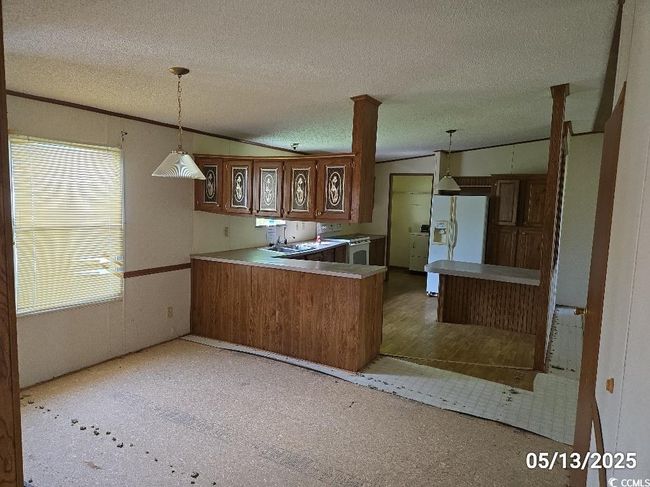 Kitchen with white fridge with ice dispenser, a peninsula, decorative light fixtures, washing machine and dryer, and a textured ceiling | Image 24