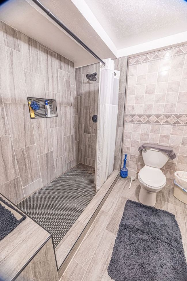 Bathroom featuring tile walls, tile patterned floors, toilet, and curtained shower | Image 35