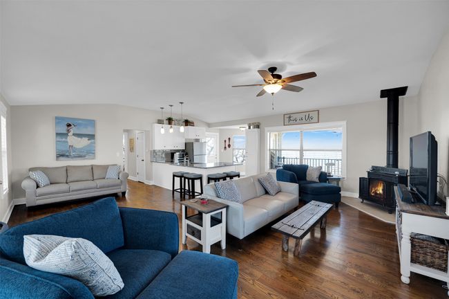 Living room featuring a ceiling fan, vaulted ceiling, a wood stove, baseboards, and dark wood-type flooring | Image 5