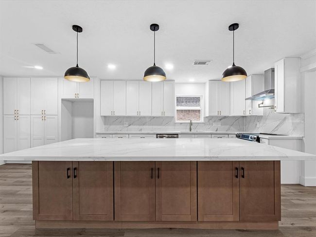 This modern kitchen features a spacious marble island, sleek white cabinets, and stainless steel appliances. Pendant lights add a stylish touch, while ample storage and counter space enhance functionality. | Image 11