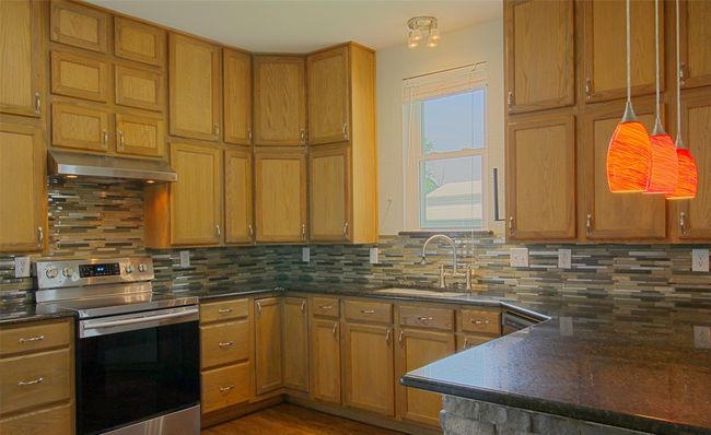 Kitchen featuring under cabinet range hood, backsplash, dark countertops, a sink, and stainless steel electric range oven | Image 8