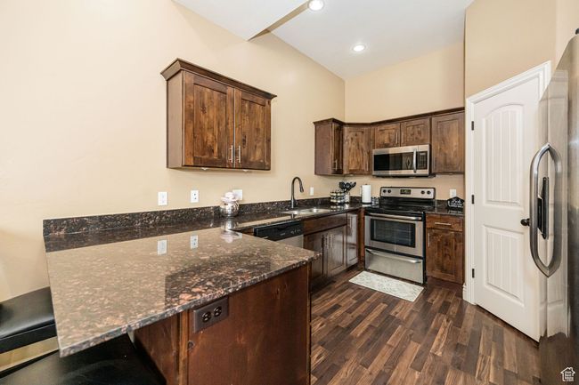 Kitchen with stainless steel appliances, dark stone countertops, a sink, dark wood-type flooring, and dark brown cabinetry | Image 12