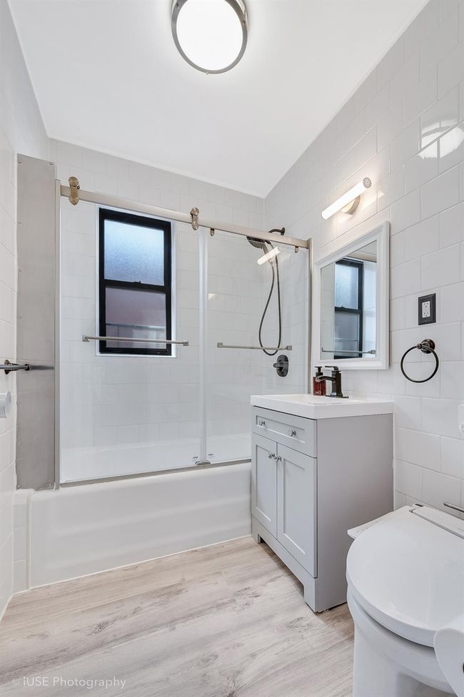 Bathroom with shower / bath combination with glass door, wood finished floors, toilet, vanity, and tile walls | Image 9