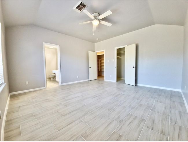 Unfurnished bedroom featuring lofted ceiling, a spacious closet, light wood-style flooring, connected bathroom, and a ceiling fan | Image 6