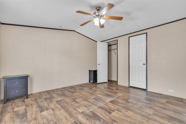 Unfurnished bedroom featuring lofted ceiling, wood finished floors, ornamental molding, a textured ceiling, and ceiling fan | Image 7