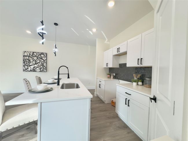 Kitchen with a kitchen island with sink, a sink, tasteful backsplash, white cabinetry, and pendant lighting | Image 9