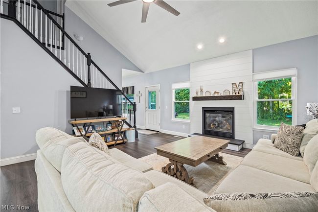 Living room with high vaulted ceiling, ceiling fan, a large fireplace, and dark wood-type flooring | Image 7