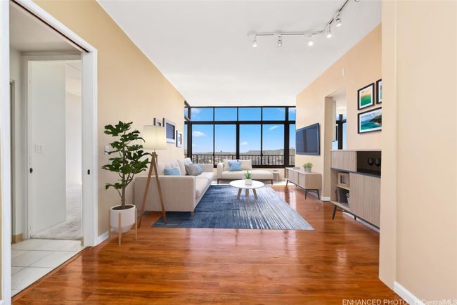 Enhanced. Virtually staged. Enclosed lanai is in background and runs the width of the condo. Kitchen is at right located behind the wall with television with entry from living area and enclosed lanai. | Image 7