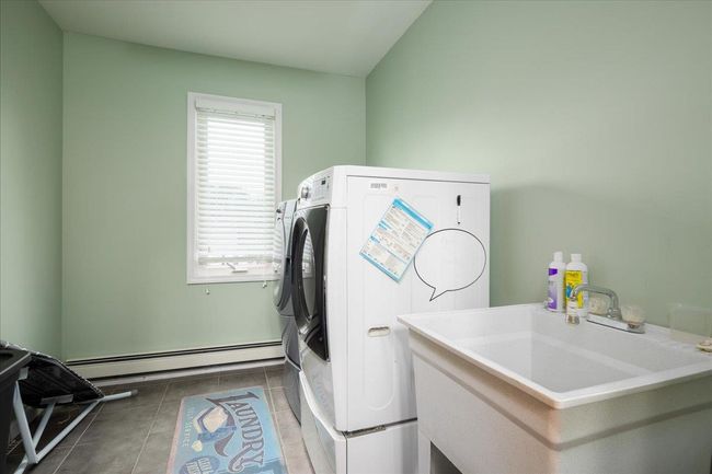 Laundry area with a baseboard heating unit, independent washer and dryer, and dark tile patterned flooring | Image 18