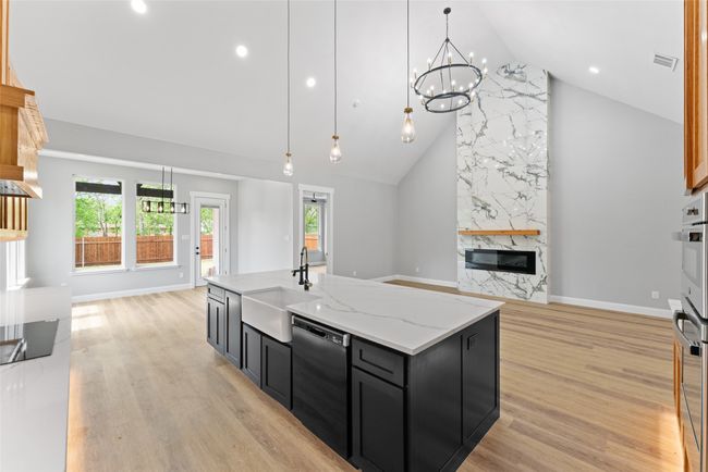 Kitchen featuring a sink, dishwasher, dark cabinetry, a premium fireplace, and high vaulted ceiling | Image 9