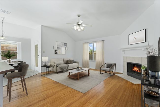 Living room with lofted ceiling, a ceiling fan, a tiled fireplace, and light wood-type flooring | Image 7