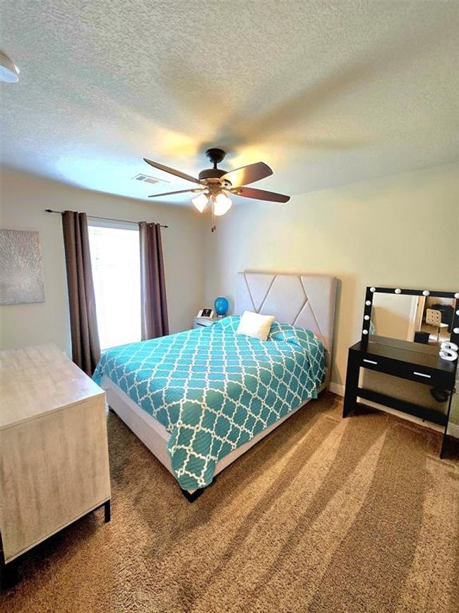 Cozy bedroom with plush carpet, featuring a ceiling fan, natural light from a large window. | Image 22