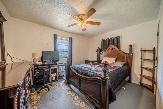 Bedroom featuring a desk, a textured ceiling, concrete flooring, and ceiling fan | Image 19