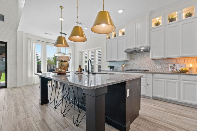 Kitchen with backsplash, a kitchen island with sink, light wood-style floors, exhaust hood, and white cabinetry | Image 10