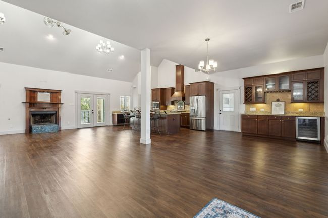 Unfurnished living room with high vaulted ceiling, dark wood-type flooring, a chandelier, and beverage cooler | Image 5