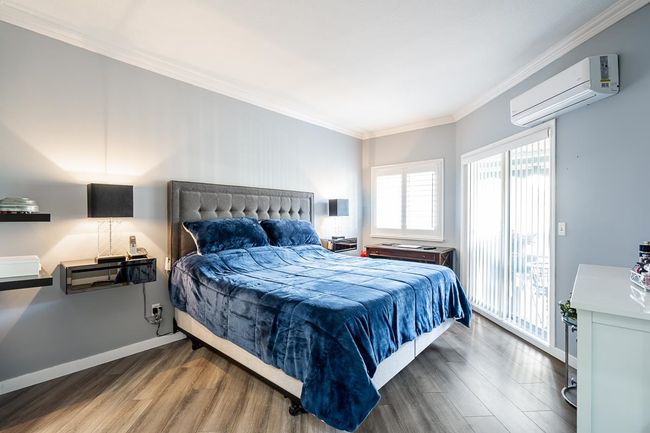 Bedroom with a wall mounted air conditioner, wood finished floors, crown molding, and access to exterior | Image 14