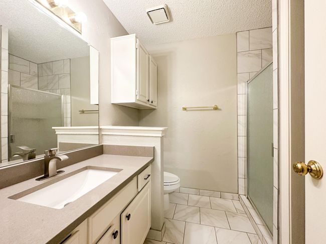 Bathroom with toilet, marble look tiles, a textured ceiling, a tile shower, and vanity | Image 10