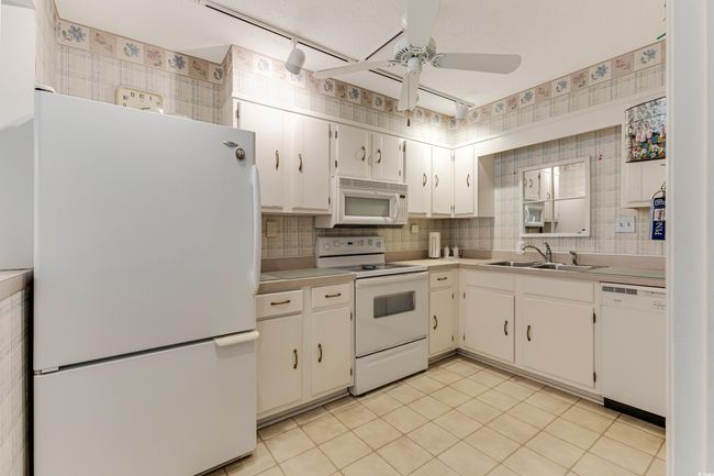 Kitchen featuring light countertops, white appliances, wallpapered walls, a sink, and a ceiling fan | Image 5