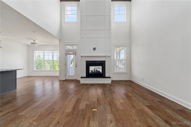 Unfurnished living room with a high ceiling, plenty of natural light, a multi sided fireplace, and wood finished floors | Image 7
