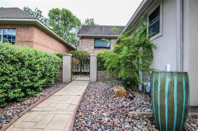 The photo shows a neatly presented side yard of a brick house, featuring a tidy walkway, a decorative fountain, lush greenery, and a wrought-iron gate leading to the backyard, creating a private and inviting outdoor space. | Image 3