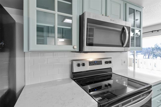 Kitchen with backsplash, a textured ceiling, appliances with stainless steel finishes, and glass insert cabinets | Image 14