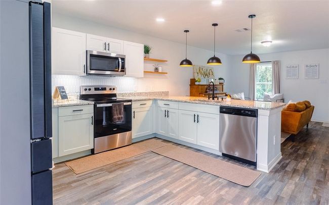 Kitchen with stainless steel appliances. There is a tankless reverse osmosis filter under the sink with filter replacements that convey with the home. Enjoy the natural wood accent shelving which is right on trend. The pendant lights have been added as well and are part of the smart lighting. Yes, they are dimmable for that perfect evening ambiance! | Image 8
