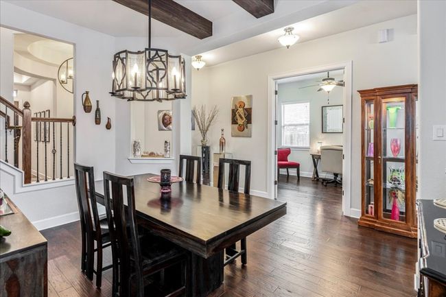 Dining space featuring dark wood-style floors, beamed ceiling, stairs, a chandelier, and ceiling fan | Image 12