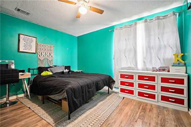 Bedroom with a textured ceiling, a ceiling fan, baseboards, wood finished floors, and visible vents | Image 15