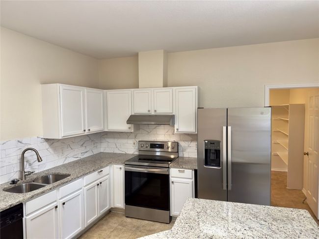 Kitchen with stainless steel appliances, white cabinetry, light tile patterned floors, and backsplash | Image 4