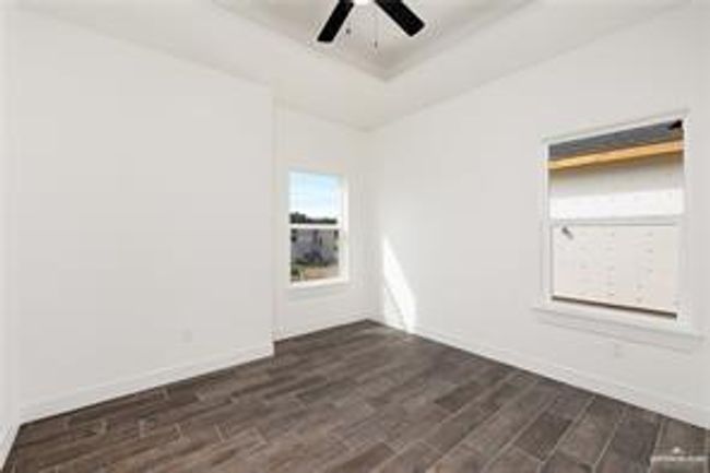 Unfurnished room featuring baseboards, a tray ceiling, ceiling fan, and dark wood-style flooring | Image 10