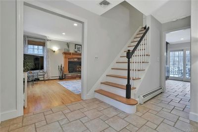 Stairway with hardwood / wood-style floors, a baseboard radiator, ornamental molding, and a brick fireplace | Image 2