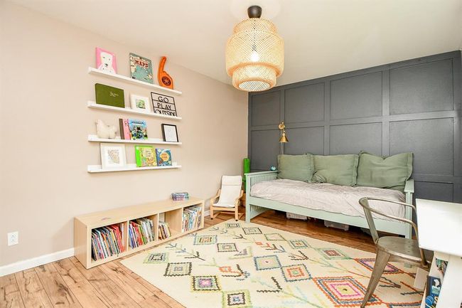 This cozy children's room features a stylish dark accent wall, a comfortable daybed with green cushions, and a playful, colorful rug. It includes wall-mounted shelves displaying books and decor, a low bookcase, and a modern woven light fixture, creating a welcoming and functional space. | Image 32
