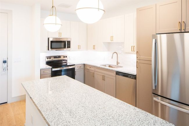 Kitchen with decorative backsplash, light wood-style flooring, light stone counters, stainless steel appliances, and a sink | Image 11