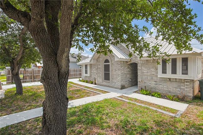 View of front facade with metal roof, brick siding, a front lawn, and fence | Image 4
