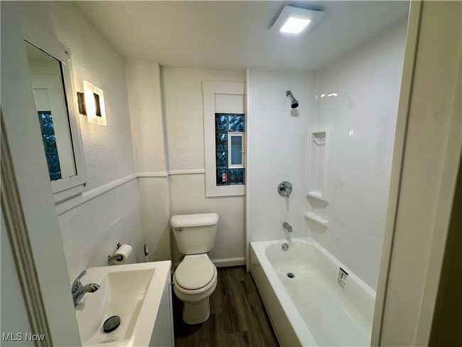 Bathroom featuring toilet, shower / bathing tub combination, wood finished floors, a textured wall, and vanity | Image 16