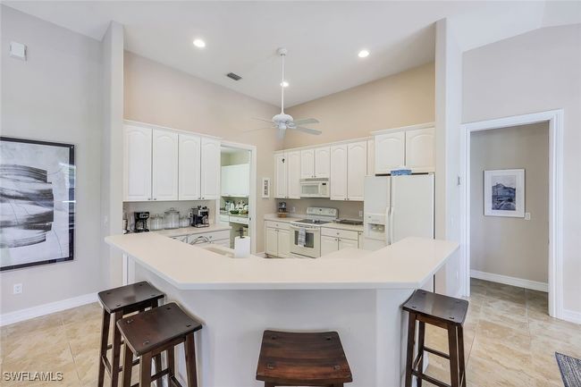 Kitchen featuring ceiling fan, white appliances, a breakfast bar area, and white cabinetry | Image 10