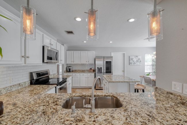 Kitchen with appliances with stainless steel finishes, light stone counters, tasteful backsplash, white cabinets, and recessed lighting | Image 5