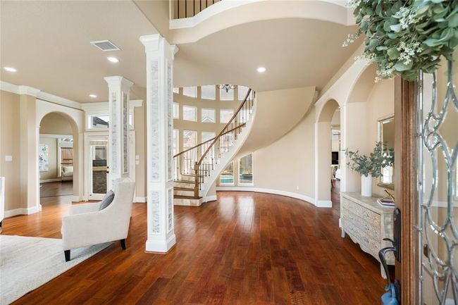 Step inside the home and you’re immediately greeted by a breathtaking view from the grand entryway. Sunlight pours through tall windows, drawing your eye toward the elegant double front doors. With soaring ceilings, graceful archways, and warm natural tones, the space sets a luxurious yet welcoming tone from the moment you arrive. | Image 11