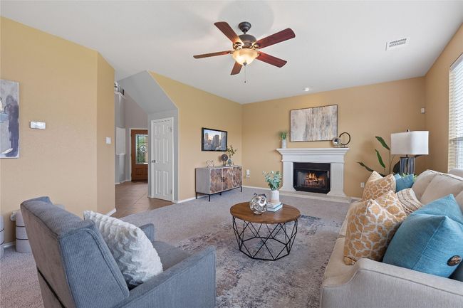 Tiled living area featuring a ceiling fan, a glass covered fireplace, and carpet flooring | Image 9