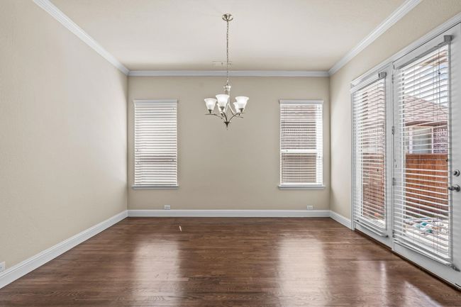 Spare room featuring healthy amount of natural light, wood finished floors, a chandelier, crown molding, and baseboards | Image 9