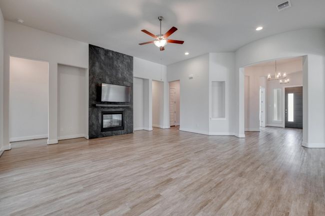 Unfurnished living room featuring a ceiling fan, a tiled fireplace, a chandelier, light wood-type flooring, and recessed lighting | Image 7