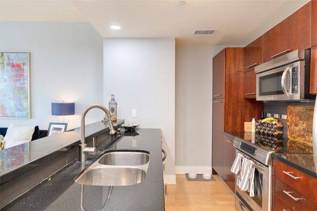 Kitchen featuring stainless steel appliances, light wood-type flooring, dark stone counters, brown cabinetry, and recessed lighting | Image 10