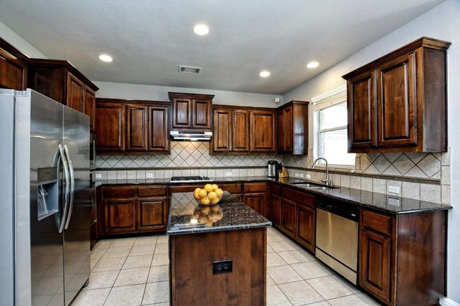 Kitchen with appliances with stainless steel finishes, under cabinet range hood, a sink, dark stone counters, and tasteful backsplash | Image 11